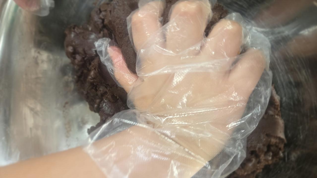장갑을 낀 아이의 손이 초코칩 반죽을 조물조물 섞고 있는 모습