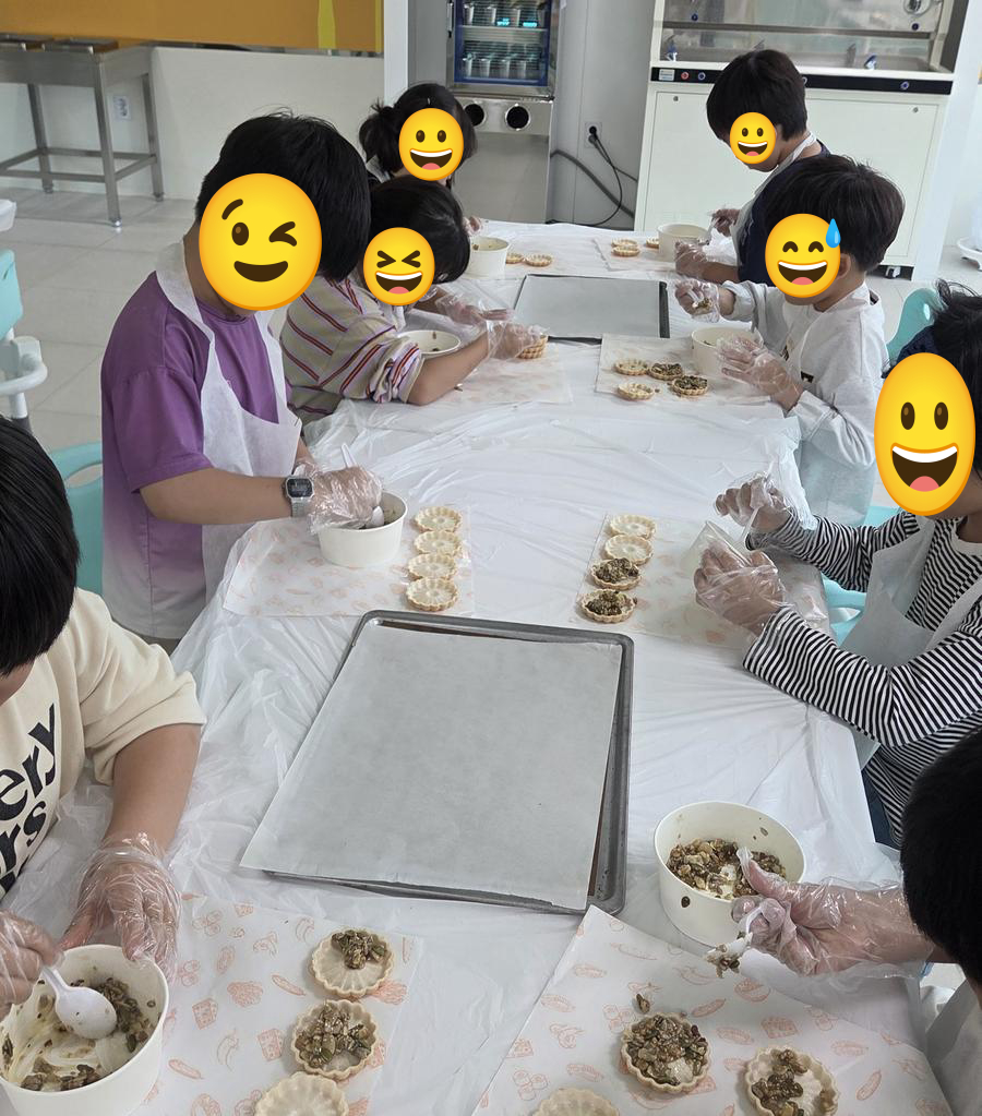 앞치마와 위생 장갑을 착용한 아이들이 스푼으로 견과류 믹스를 타르트지에 채우는 모습